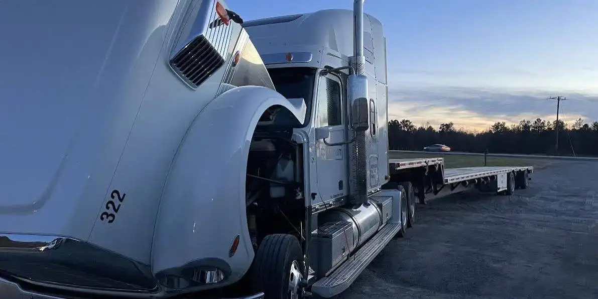 A Freightliner with its hood open beside its trailer at dusk