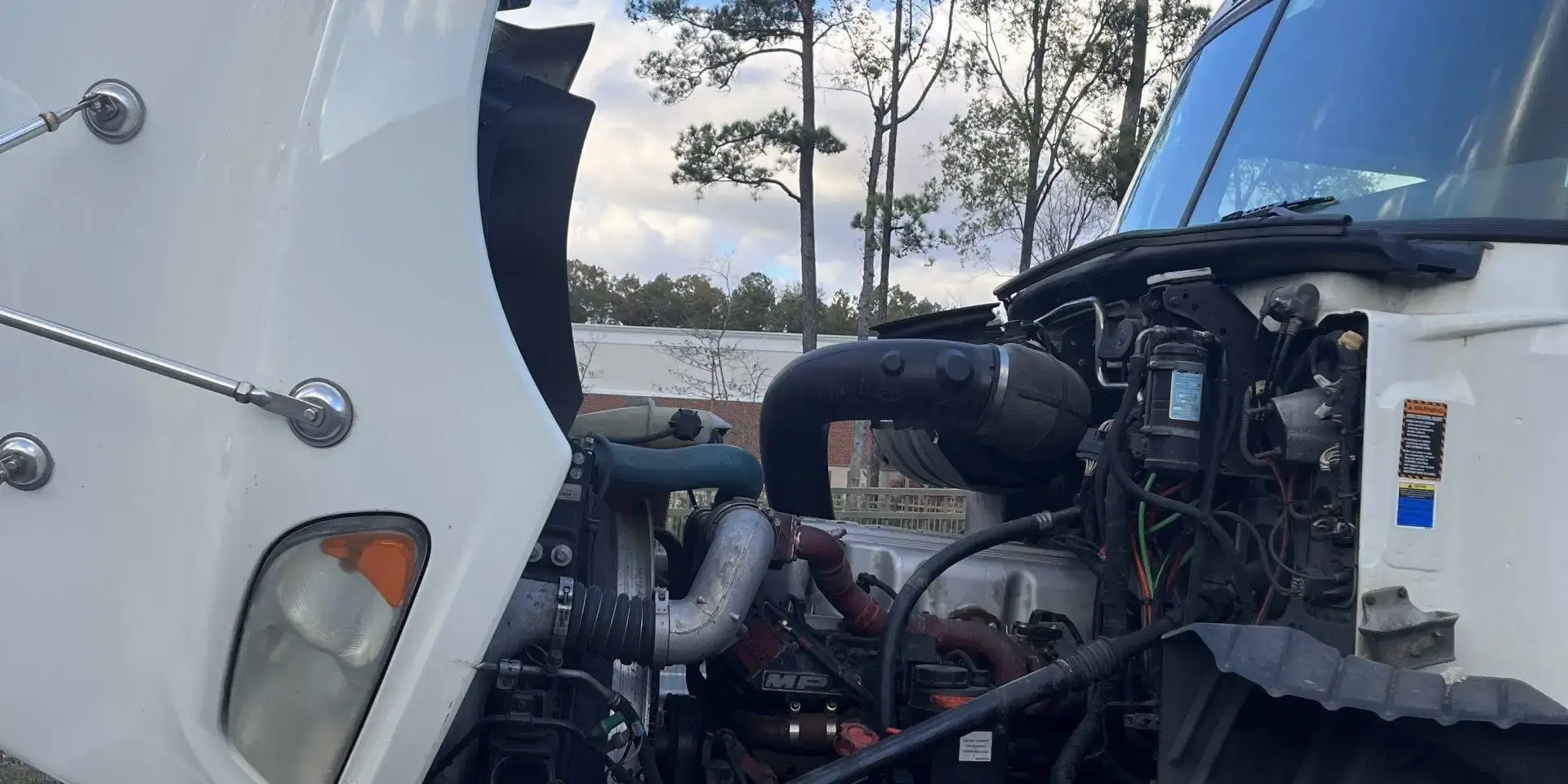 A Mack tractor with its hood tilted open for a roadside diagnosis