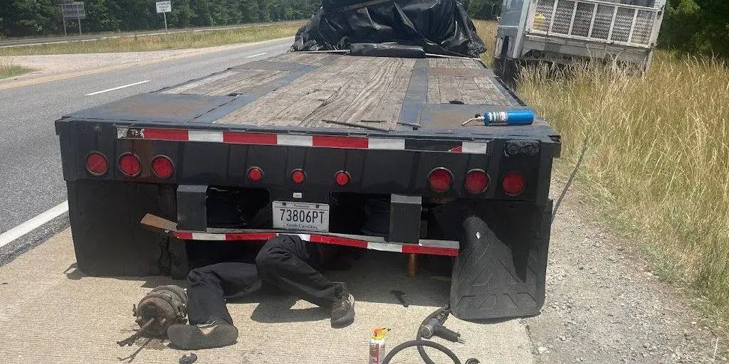 A technician working underneath a flatbed trailer on the hard shoulder
