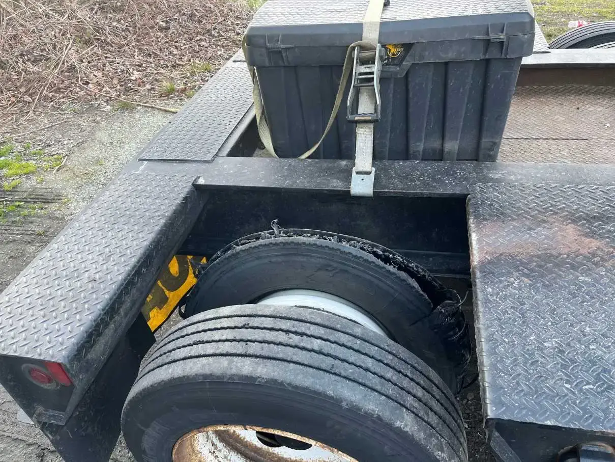 A trailer deck carrying spare wheels beside a shredded tire