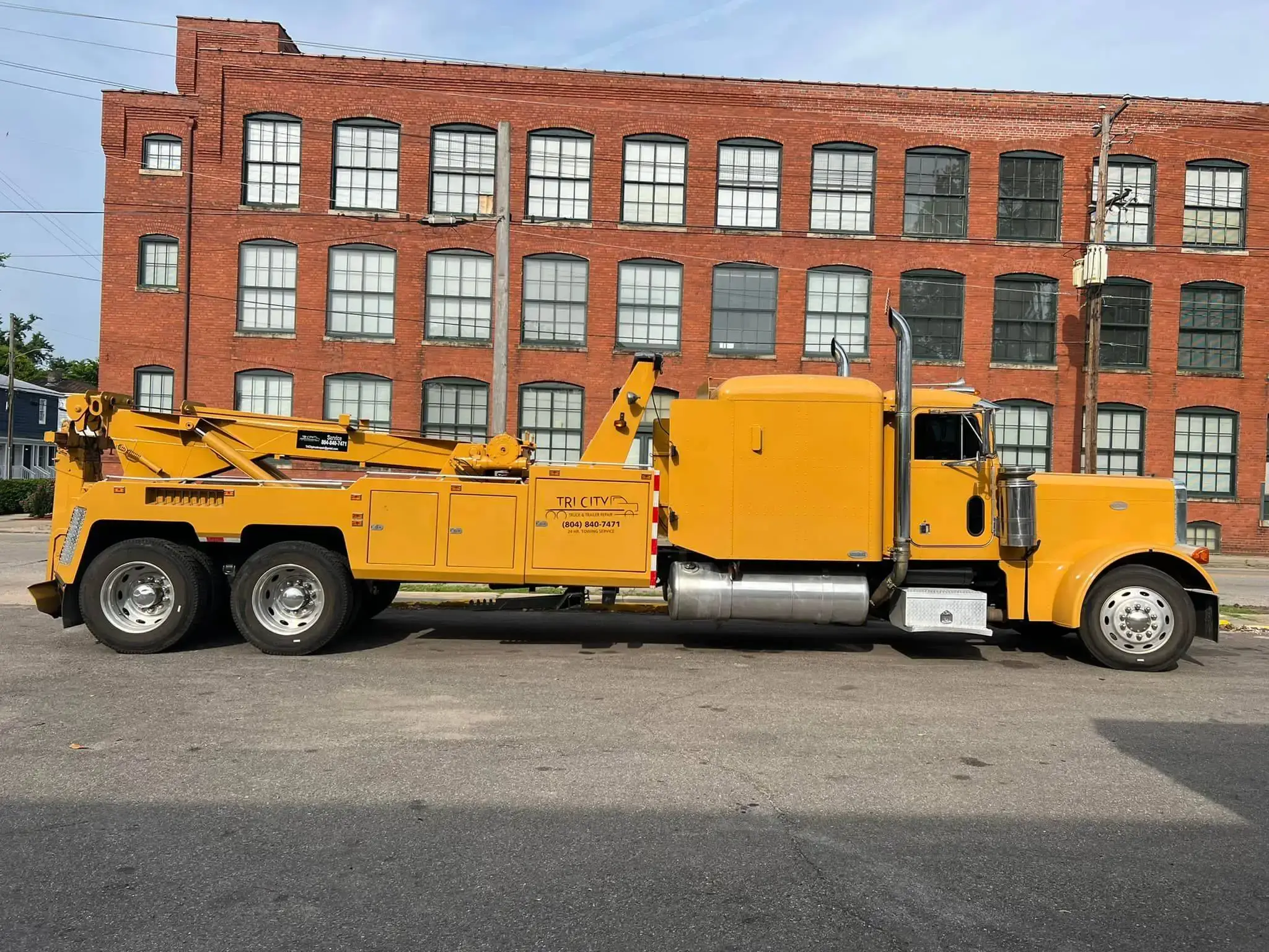 Tri City's yellow Peterbilt wrecker parked alongside a brick mill building in Petersburg