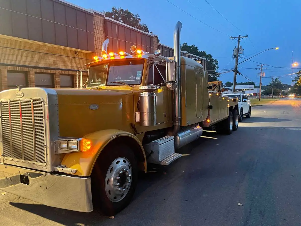 A gold Peterbilt wrecker towing an SUV at dusk